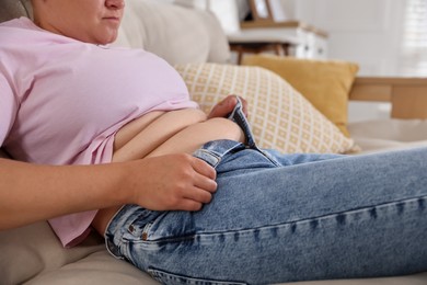 Photo of Overweight woman trying to put on tight jeans at home, closeup