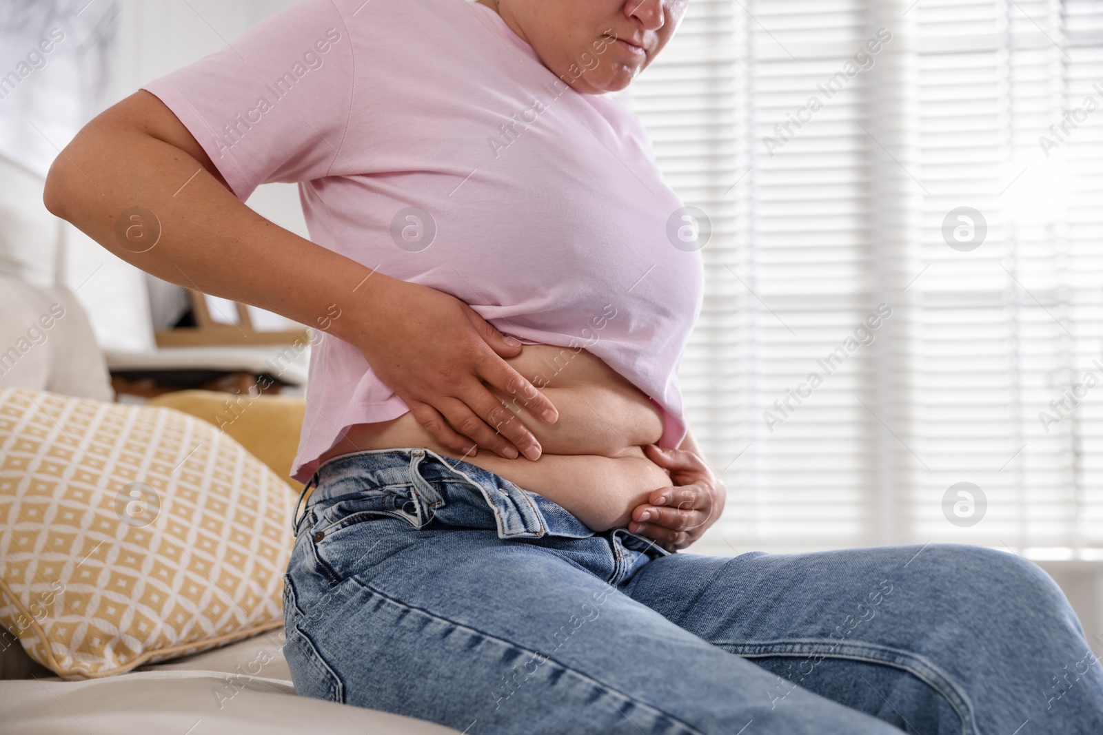 Woman with excessive belly fat at home, closeup. Overweight problem Photo of Woman with excessive belly fat at home, closeup. Overweight problem