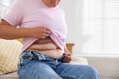 Photo of Woman with excessive belly fat at home, closeup. Overweight problem