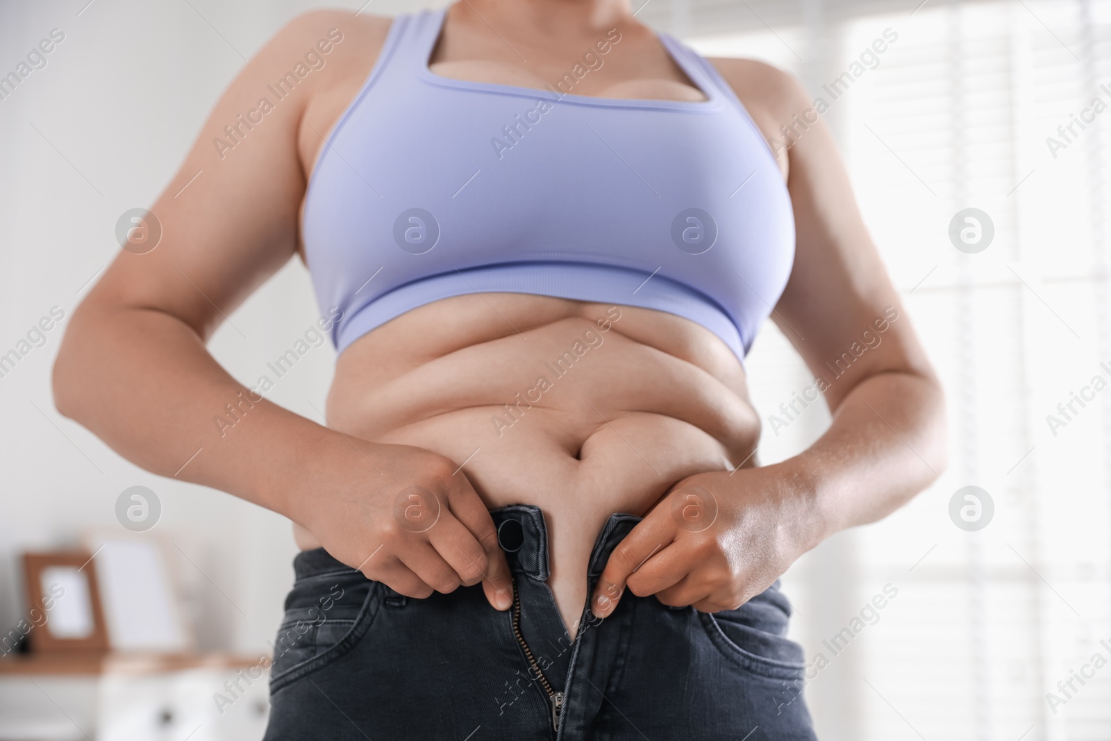 Overweight woman trying to put on tight jeans at home, closeup Photo of Overweight woman trying to put on tight jeans at home, closeup