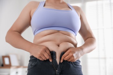 Photo of Overweight woman trying to put on tight jeans at home, closeup