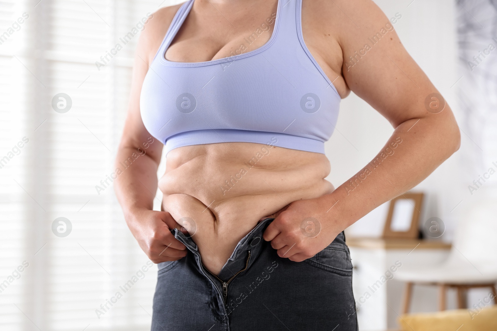 Overweight woman trying to put on tight jeans at home, closeup Photo of Overweight woman trying to put on tight jeans at home, closeup