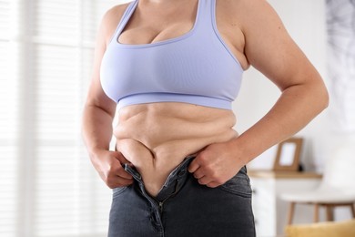 Photo of Overweight woman trying to put on tight jeans at home, closeup