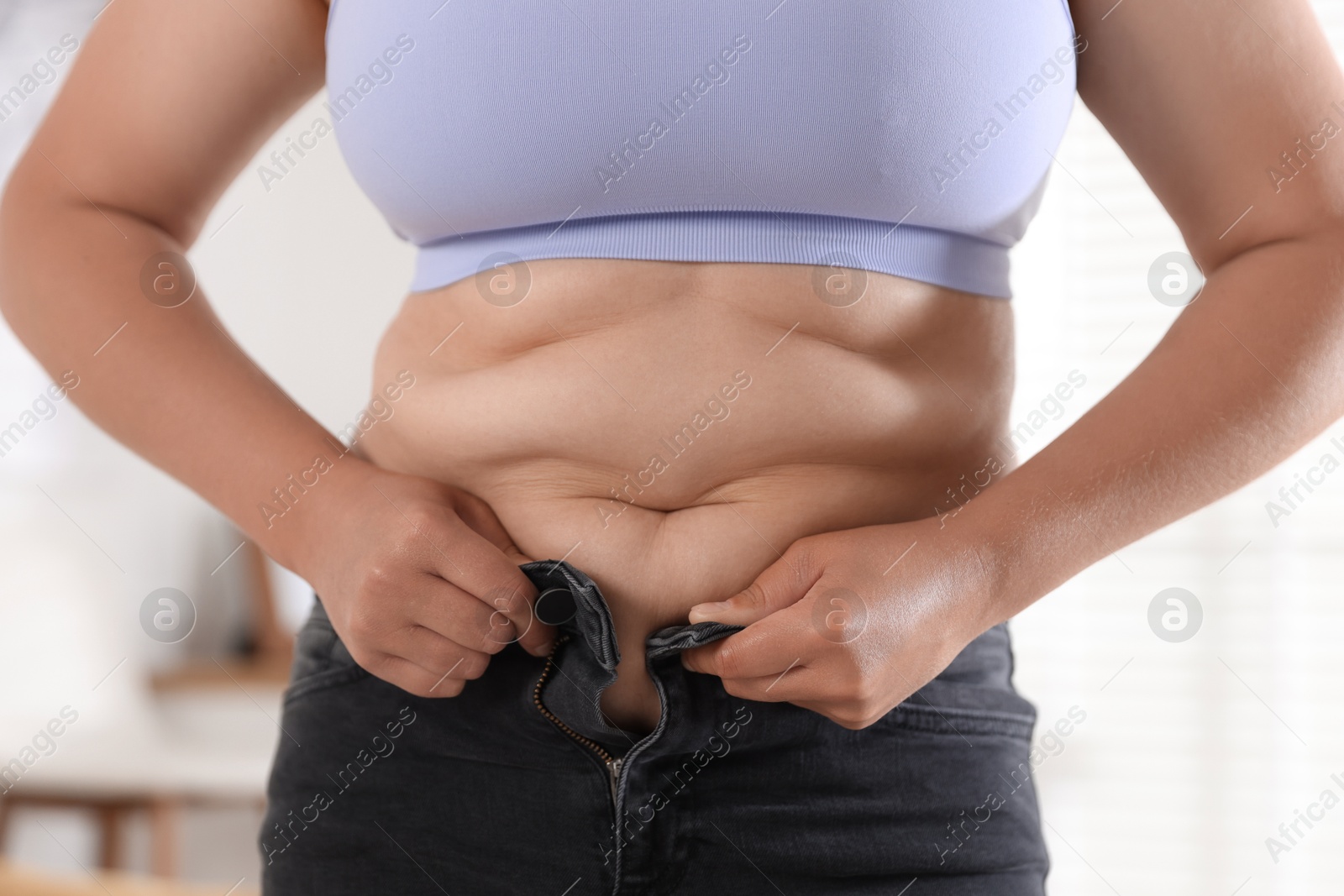 Overweight woman trying to put on tight jeans at home, closeup Photo of Overweight woman trying to put on tight jeans at home, closeup