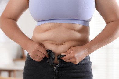 Photo of Overweight woman trying to put on tight jeans at home, closeup