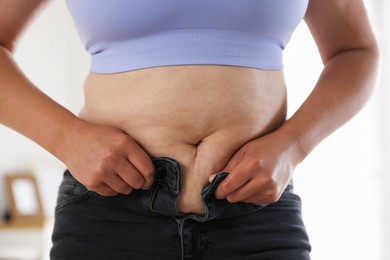 Photo of Overweight woman trying to put on tight jeans at home, closeup