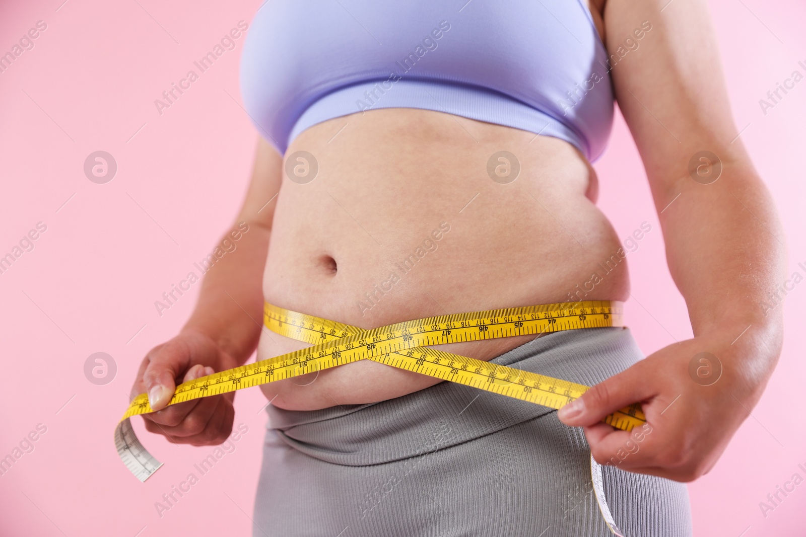 Overweight woman measuring her belly with tape on pink background, closeup Photo of Overweight woman measuring her belly with tape on pink background, closeup