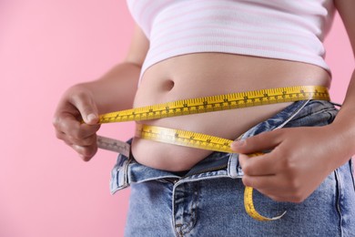 Photo of Overweight woman measuring her belly with tape on pink background, closeup