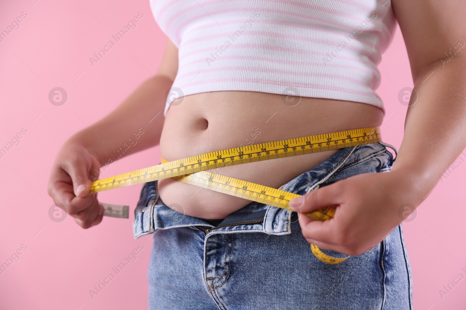 Overweight woman measuring her belly with tape on pink background, closeup Photo of Overweight woman measuring her belly with tape on pink background, closeup