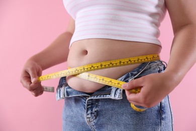 Photo of Overweight woman measuring her belly with tape on pink background, closeup