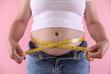 Photo of Overweight woman measuring her belly with tape on pink background, closeup
