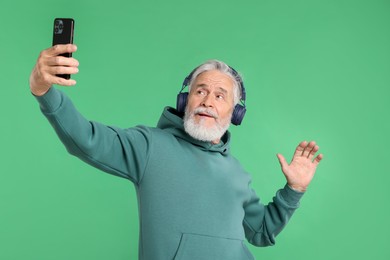 Photo of Elderly man in headphones taking selfie on green background
