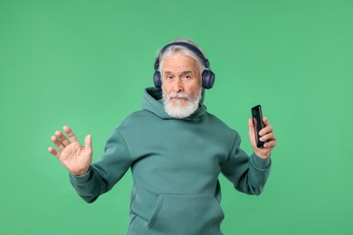 Photo of Elderly man in headphones with smartphone on green background