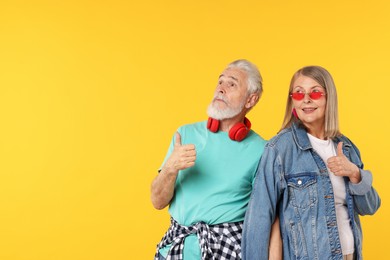 Photo of Senior couple in stylish outfits showing thumbs up on orange background, space for text