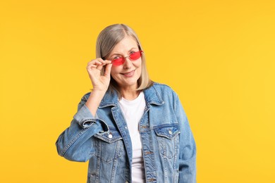 Photo of Senior woman wearing stylish sunglasses on orange background