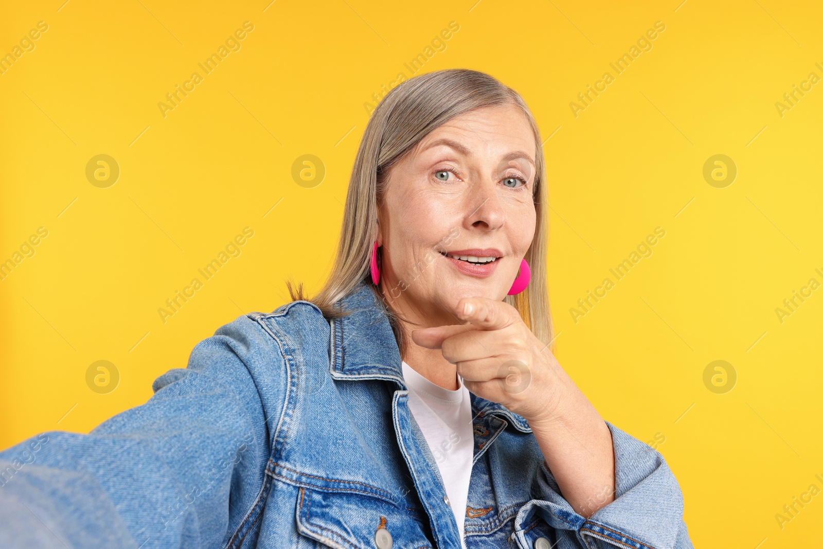 Senior woman in stylish outfit taking selfie on orange background Photo of Senior woman in stylish outfit taking selfie on orange background