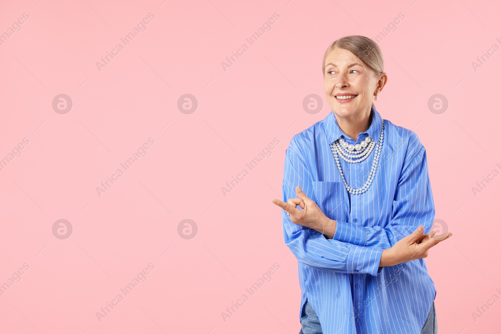 Senior woman wearing elegant pearl jewelry and making rock gesture on pink background, space for text Photo of Senior woman wearing elegant pearl jewelry and making rock gesture on pink background, space for text
