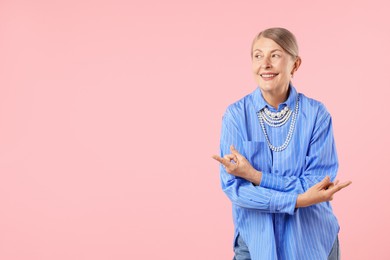 Photo of Senior woman wearing elegant pearl jewelry and making rock gesture on pink background, space for text