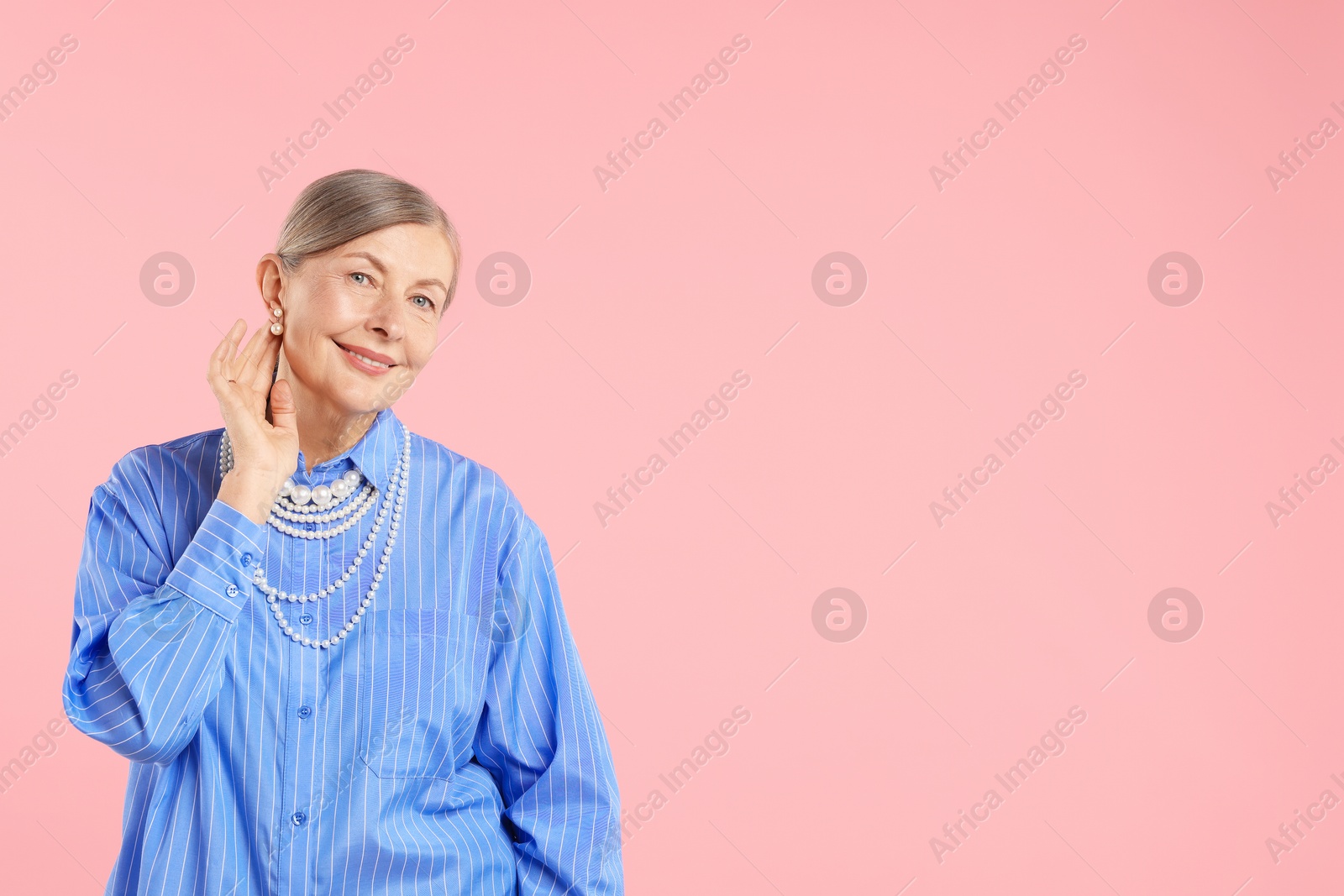 Senior woman wearing elegant pearl jewelry on pink background, space for text Photo of Senior woman wearing elegant pearl jewelry on pink background, space for text