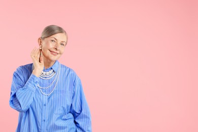Photo of Senior woman wearing elegant pearl jewelry on pink background, space for text