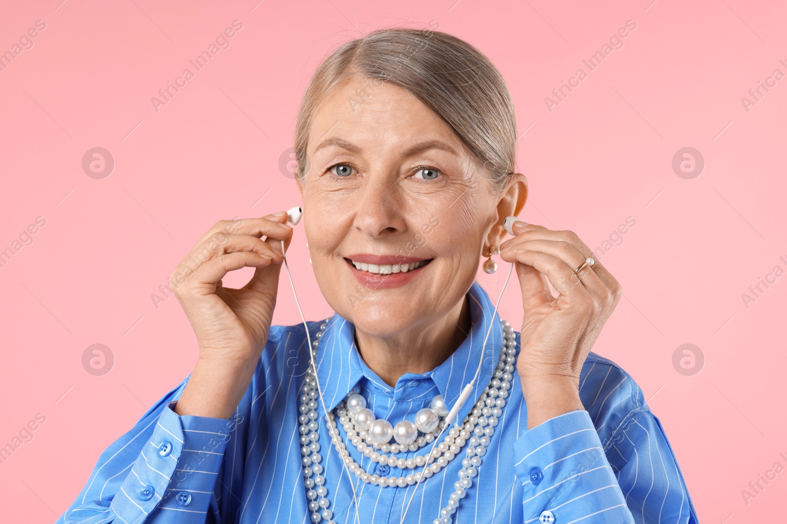 Senior woman with earphones on pink background Photo of Senior woman with earphones on pink background