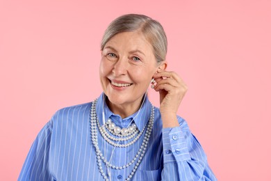 Photo of Senior woman in earphones listening to music on pink background