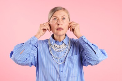 Photo of Senior woman in earphones listening to music on pink background