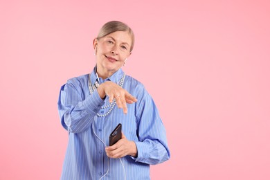Photo of Senior woman in earphones listening to music on pink background, space for text