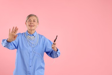 Photo of Senior woman in earphones listening to music on pink background, space for text