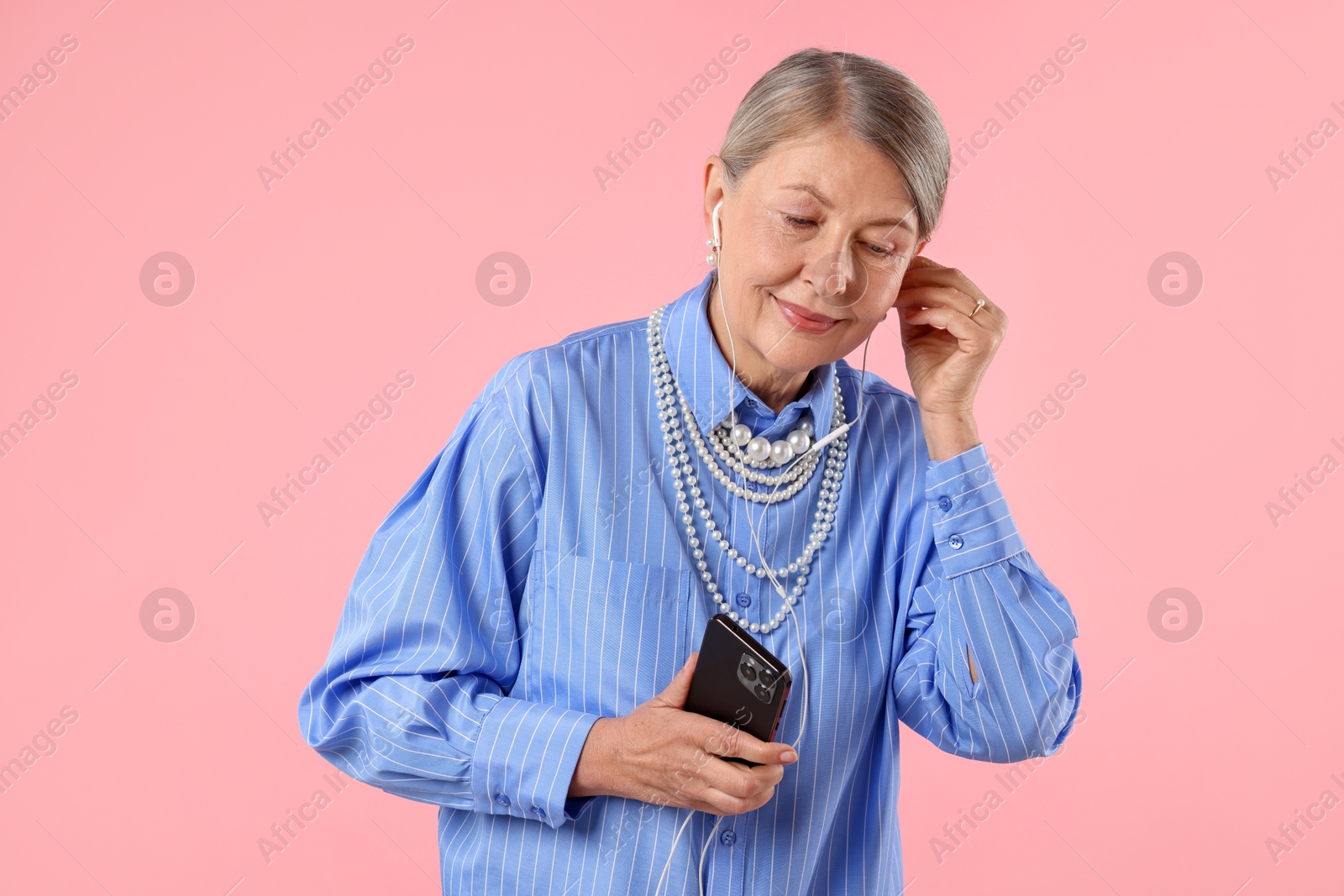 Senior woman in earphones listening to music on pink background Photo of Senior woman in earphones listening to music on pink background