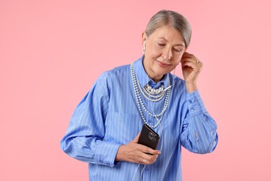 Photo of Senior woman in earphones listening to music on pink background