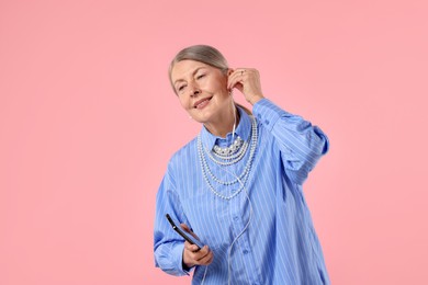 Photo of Senior woman in earphones listening to music on pink background