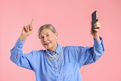 Photo of Senior woman in earphones listening to music on pink background
