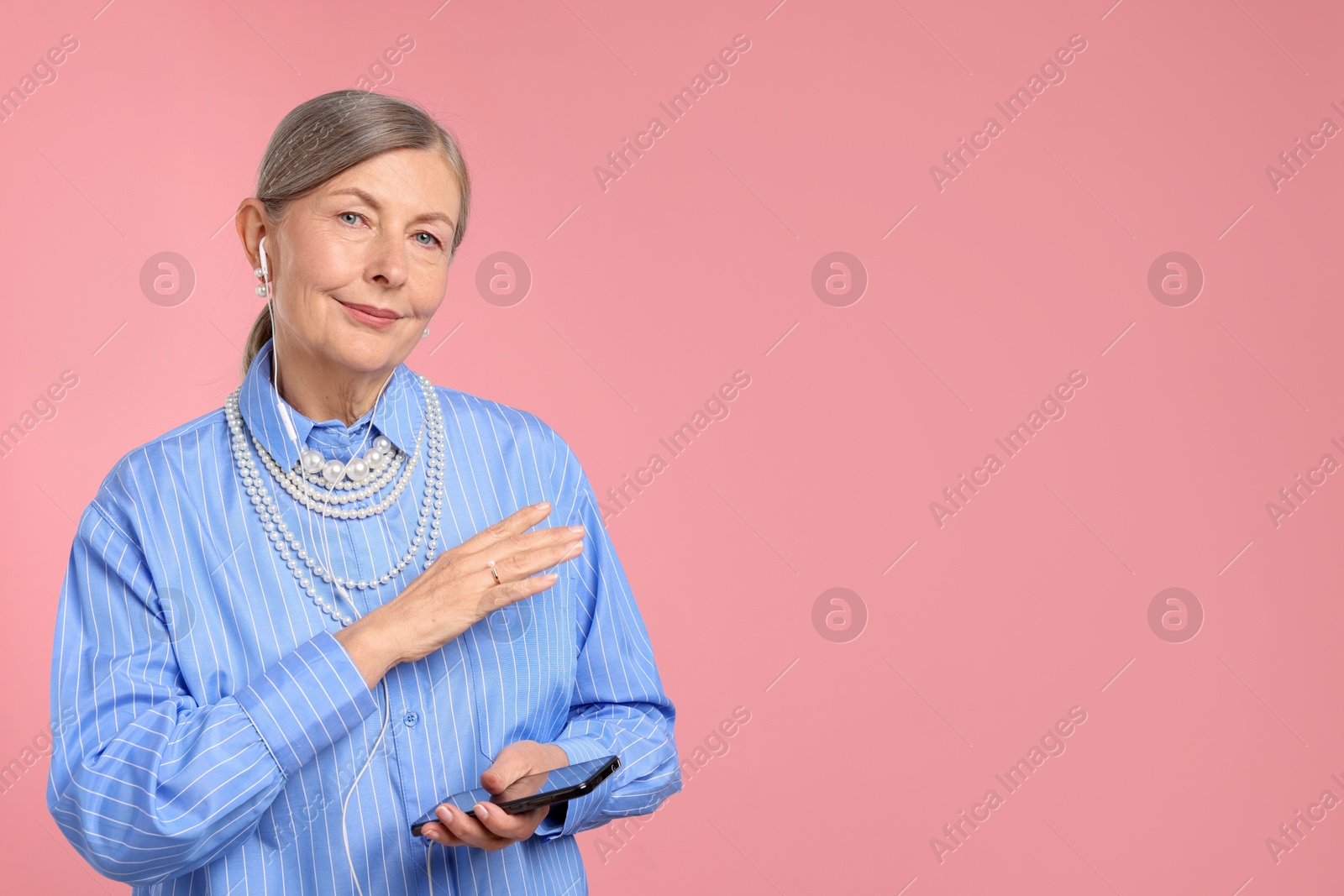 Senior woman in earphones listening to music on pink background, space for text Photo of Senior woman in earphones listening to music on pink background, space for text