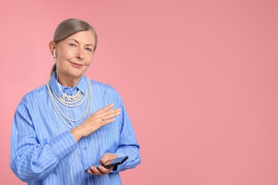 Photo of Senior woman in earphones listening to music on pink background, space for text