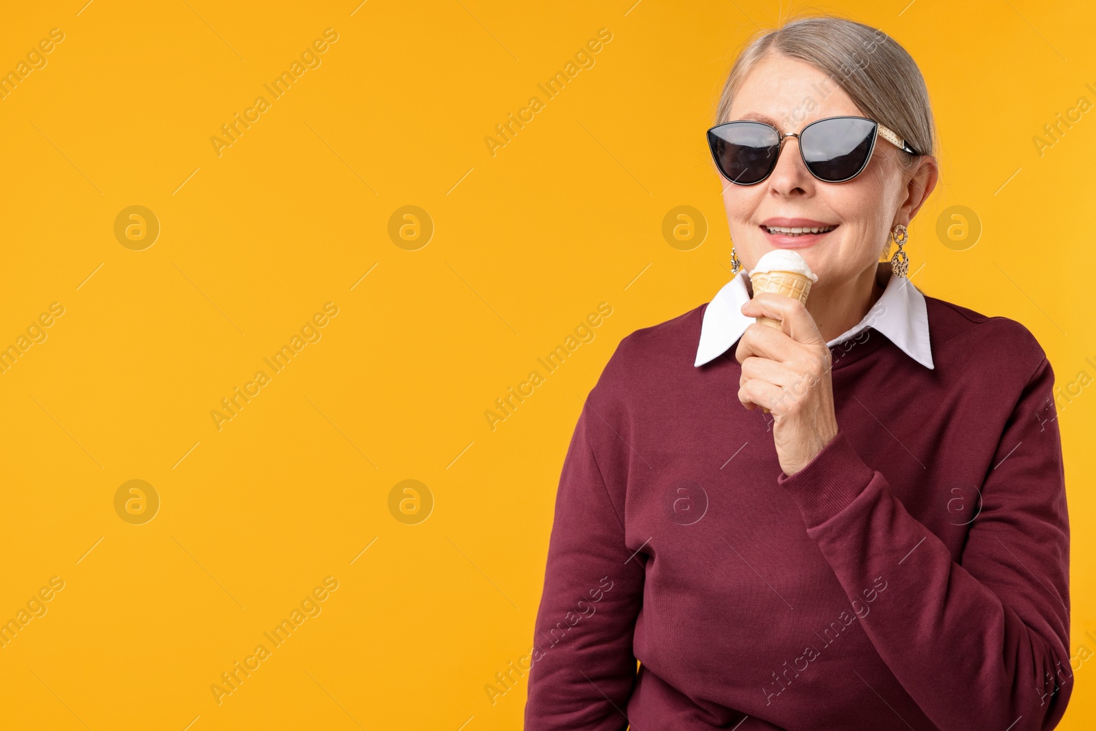 Senior woman in stylish outfit holding tasty ice cream on orange background, space for text Photo of Senior woman in stylish outfit holding tasty ice cream on orange background, space for text