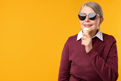 Photo of Senior woman in stylish outfit holding tasty ice cream on orange background, space for text