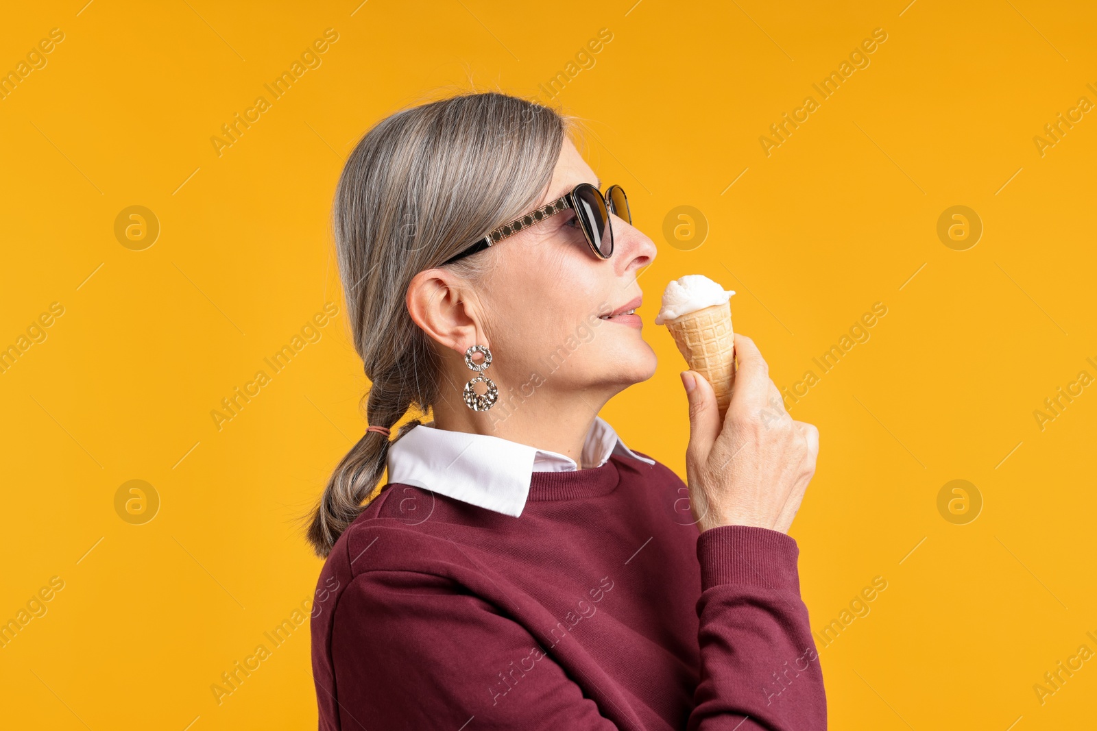Senior woman in stylish outfit holding tasty ice cream on orange background Photo of Senior woman in stylish outfit holding tasty ice cream on orange background