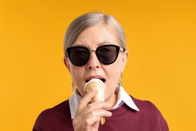 Photo of Senior woman in stylish outfit eating ice cream on orange background