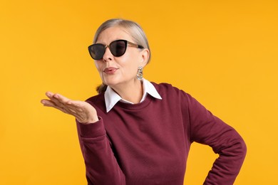 Photo of Senior woman in stylish outfit blowing kiss on orange background
