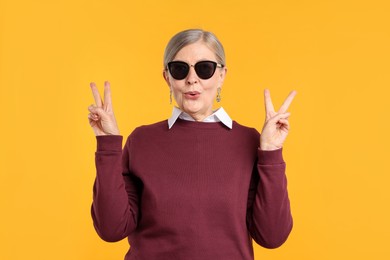 Photo of Senior woman in stylish outfit showing V-signs on orange background