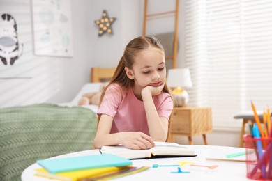 Photo of Dyslexia. Upset little girl reading book at table indoors