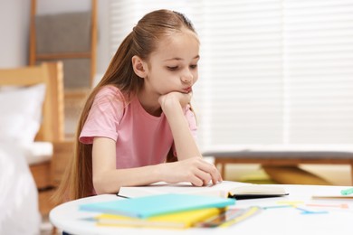 Photo of Dyslexia. Upset little girl reading book at table indoors