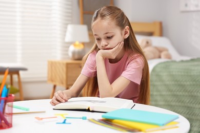 Photo of Dyslexia. Upset little girl reading book at table indoors