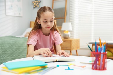 Photo of Dyslexia. Little girl reading book at table indoors