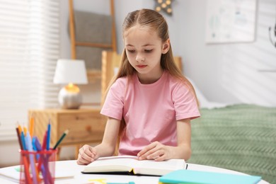 Photo of Dyslexia. Little girl reading book at table indoors