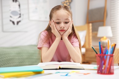 Photo of Dyslexia. Upset little girl reading book at table indoors