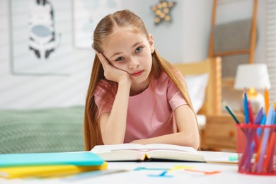 Photo of Dyslexia. Upset little girl reading book at table indoors