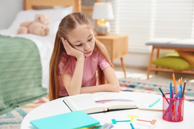 Photo of Dyslexia. Upset little girl reading book at table indoors