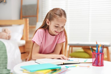 Photo of Dyslexia. Little girl reading book at table indoors